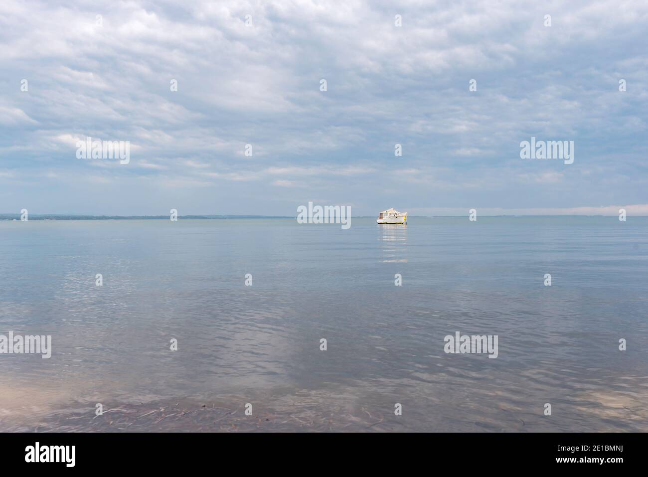 A lone white motor cruiser boat sits on glassy water in Port Stephens reflecting grey rain clouds above Stock Photo