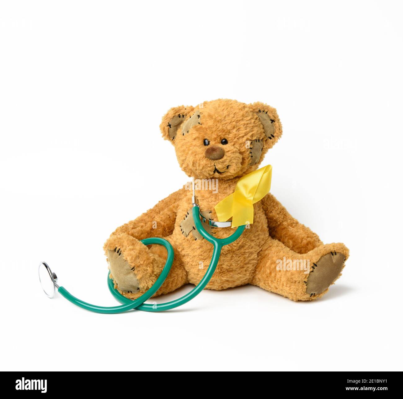 Cute brown teddy bear with a patch, a silk yellow ribbon in the shape of a loop on a white background, concept of the fight against childhood cancer, Stock Photo