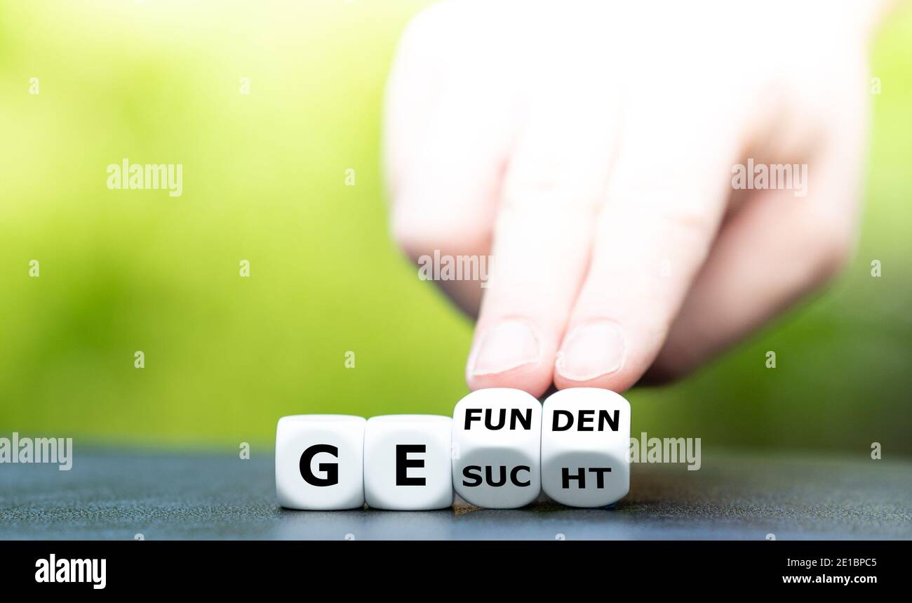 Hand turns dice and changes the German word 'gesucht' (wanted) to 'gefunden' (found). Stock Photo