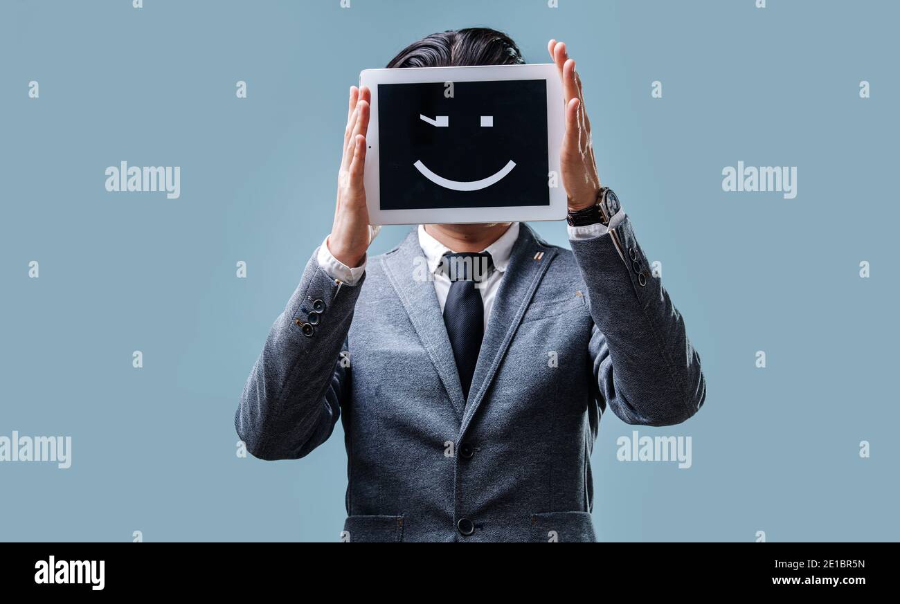 Businessman in jacket and tie holds a tablet computer with smile emoji Stock Photo