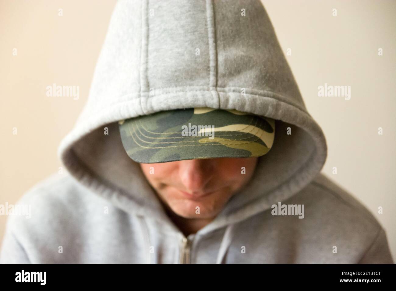 A man in a military baseball cap and a grey hooded sweatshirt, looking down Stock Photo