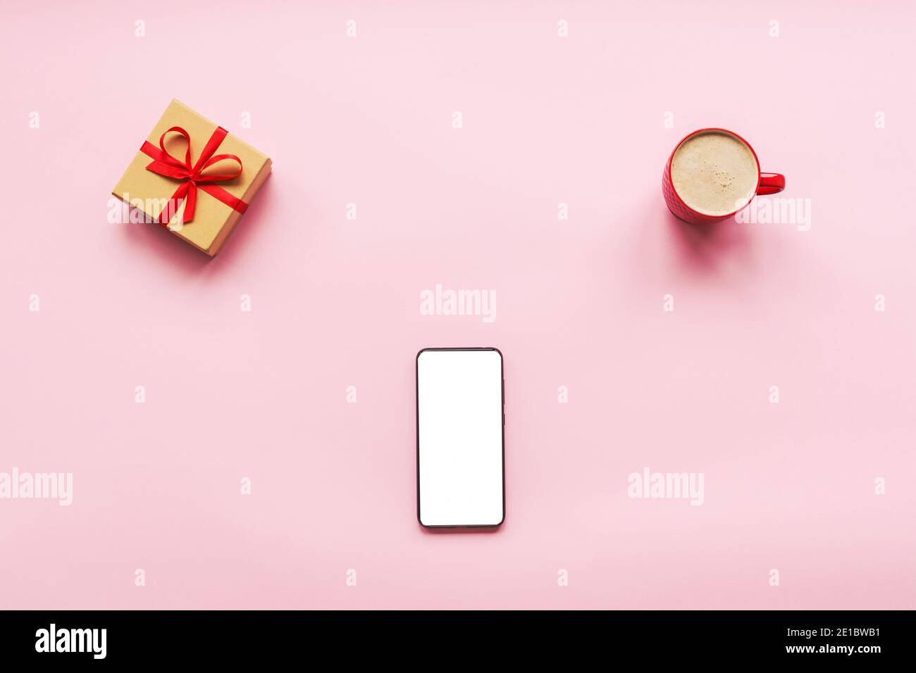 Cup of cappuccino, gift in a box and mobile phone with blank screen on a pink background. Love concept, Valentines day. Top view, flat lay. Stock Photo