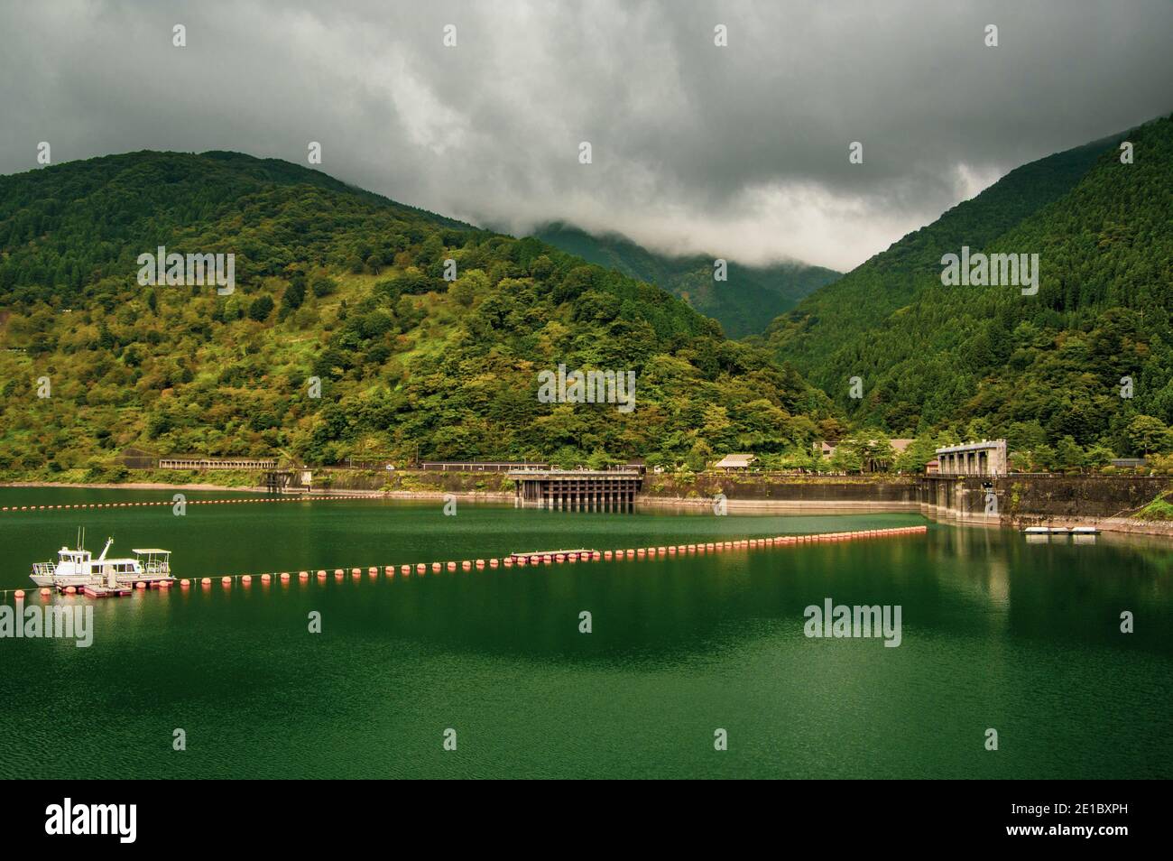 Low-lying clouds slowly creep over the mountain peaks as the enter the village below. View of Okutama Lake looking northwest form atop Ogouchi Dam. Th Stock Photo