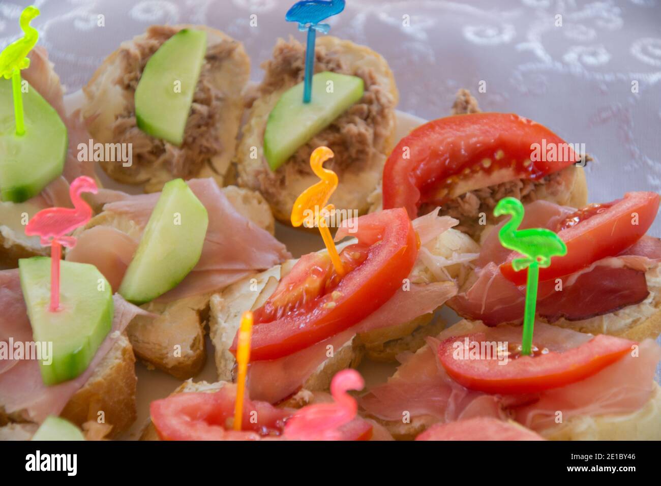 Healthy sandwiches with ham, tomato and cucumbers on a plate, decorated with plastic sticks with colorful flamingos, party concepts, appetizers Stock Photo