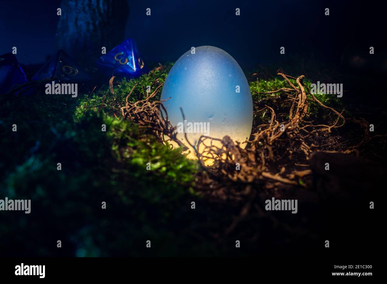Close-up rpg scene of a white opaque egg in a nest of moss, dirt and roots. With in the background three 8 sided dice. Stock Photo