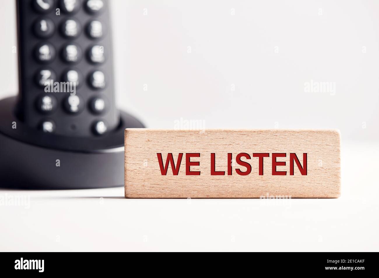 The word we listen on wooden block with telephone background. Business concept for customer assistance or service. Stock Photo