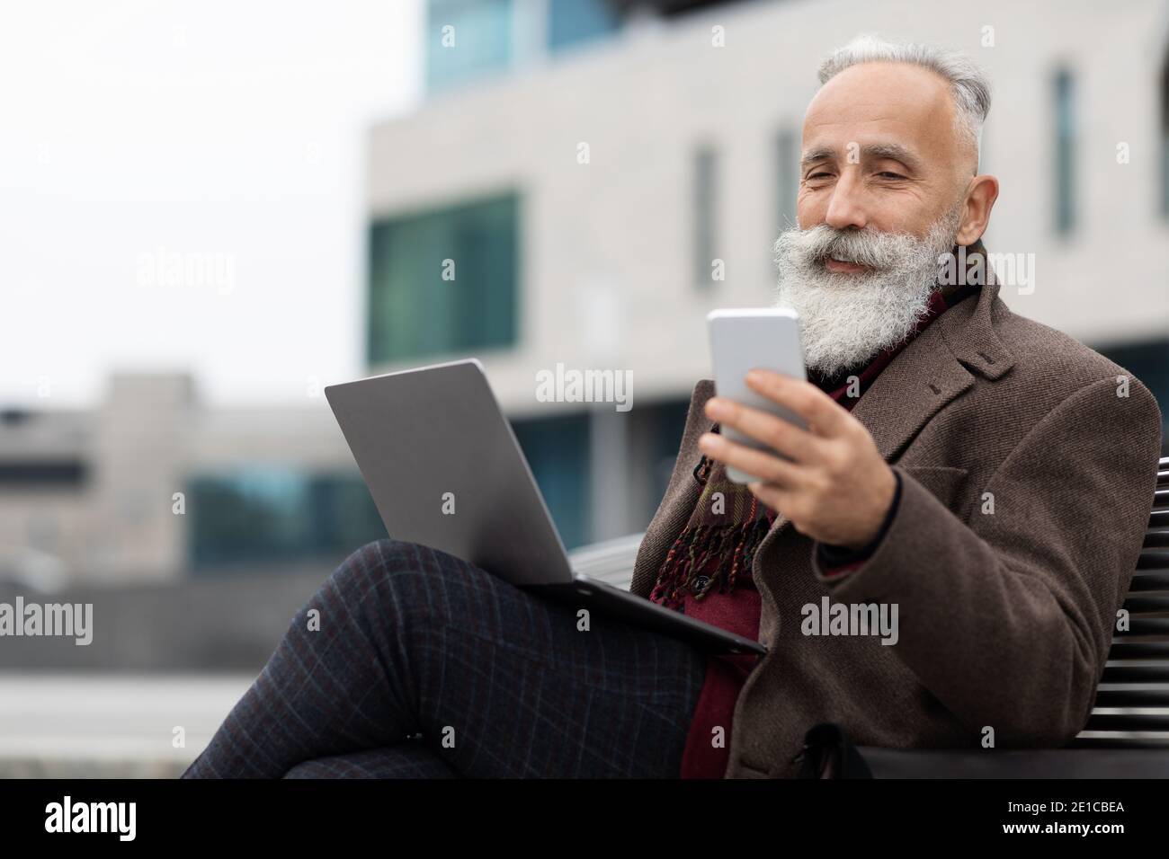 Senior businessman with laptop using smartphone outdoors Stock Photo