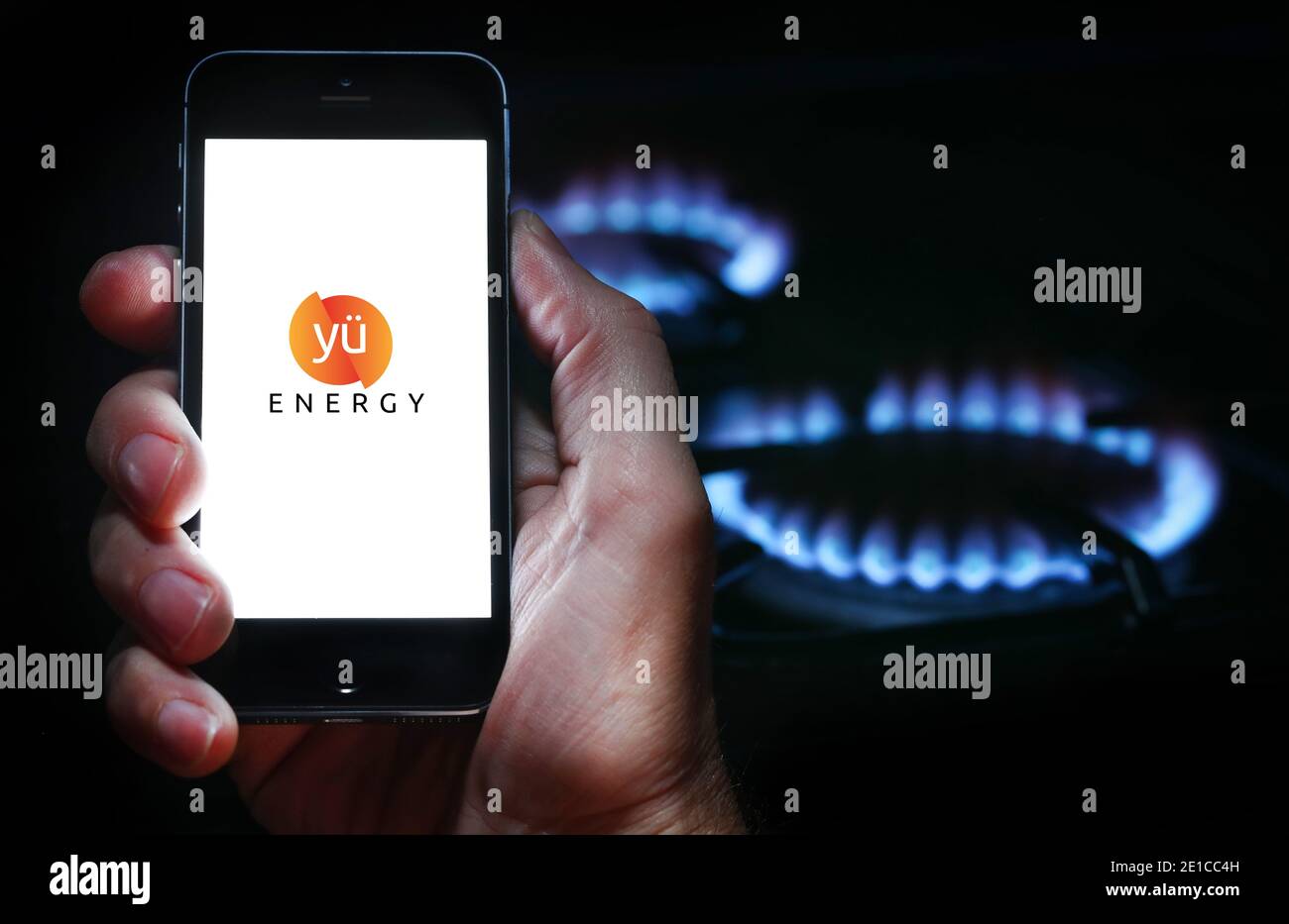 A man looking at the website logo for energy company Yu Energy on his phone in front of his gas cooker (editorial use only) Stock Photo