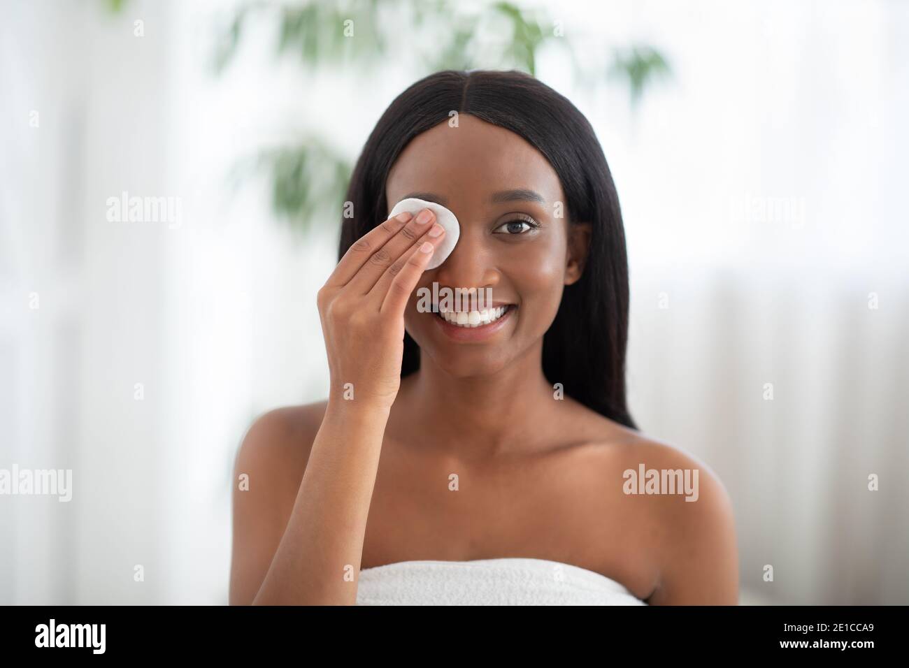 Cheerful african american lady cleanses skin with cotton pad and cosmetics product for properly deep clean Stock Photo