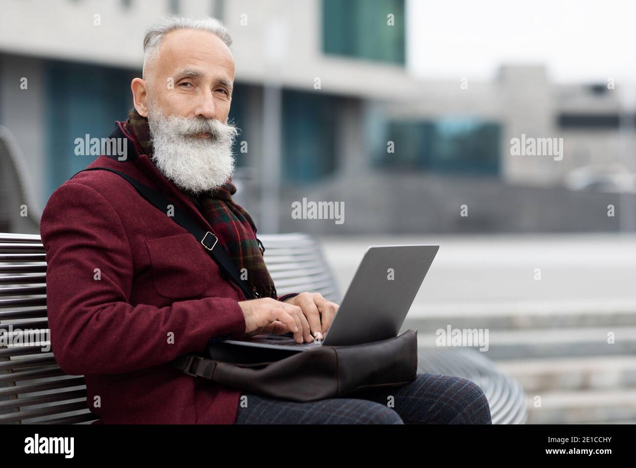 Modern grandfather using laptop while sitting on bench Stock Photo