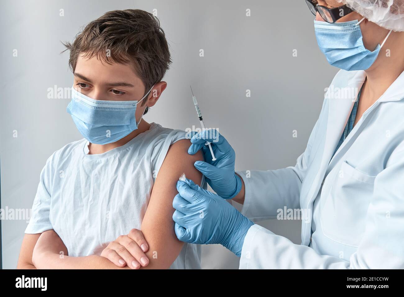 Close-up on hands in gloves with syringe and shoulder of the patient, teen kid. Covid 19, flu, tetanus or measles vaccine concept. Medic, doctor or Stock Photo