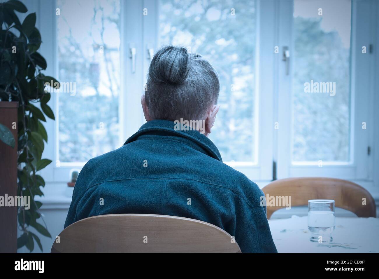 Loneliness concept, old-age depression: lonely old woman looking out of the window, blue filter effect. Stock Photo