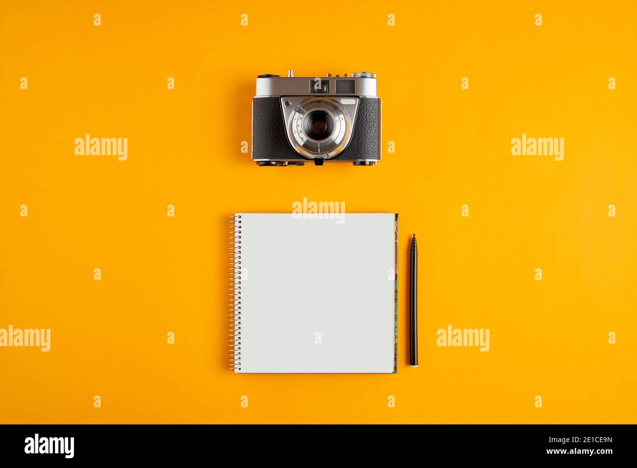 Vintage analog camera with a spiral blank notebook against yellow background with copy space. Stock Photo