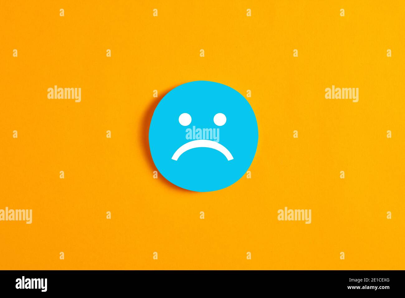Blue round circle with a sad face icon against yellow background. Negative expression or customer dissatisfaction in business concept. Stock Photo