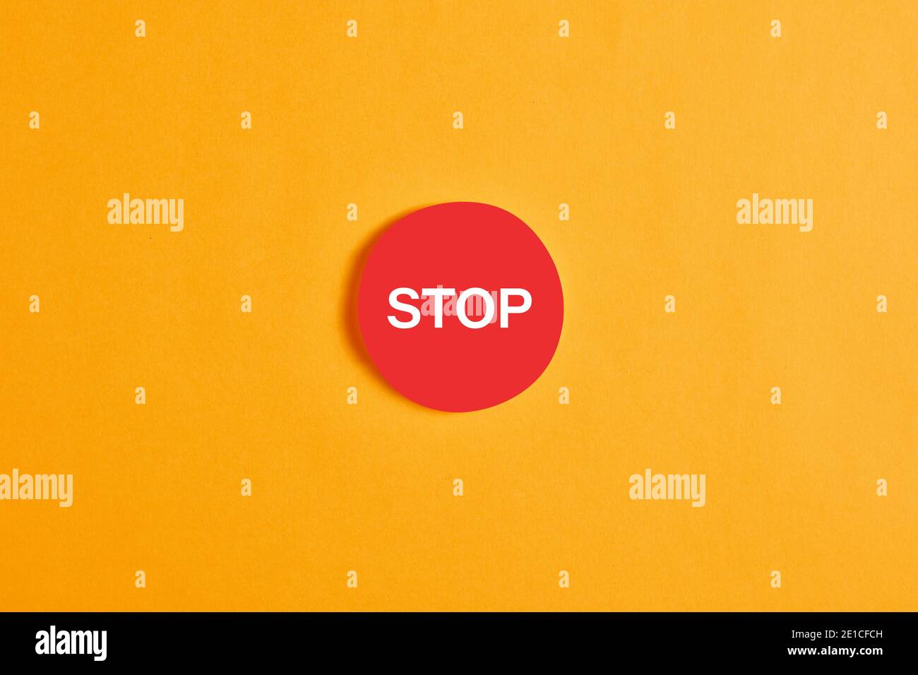 Red round button with the word stop against yellow background. Stock Photo
