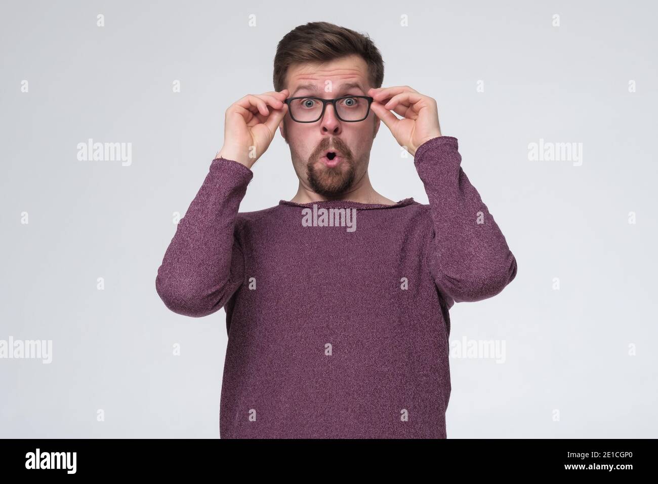 Wow, it can not be. Surprised young man with opened mouth touching glasses. I do not belive my eyes. Studio shot Stock Photo