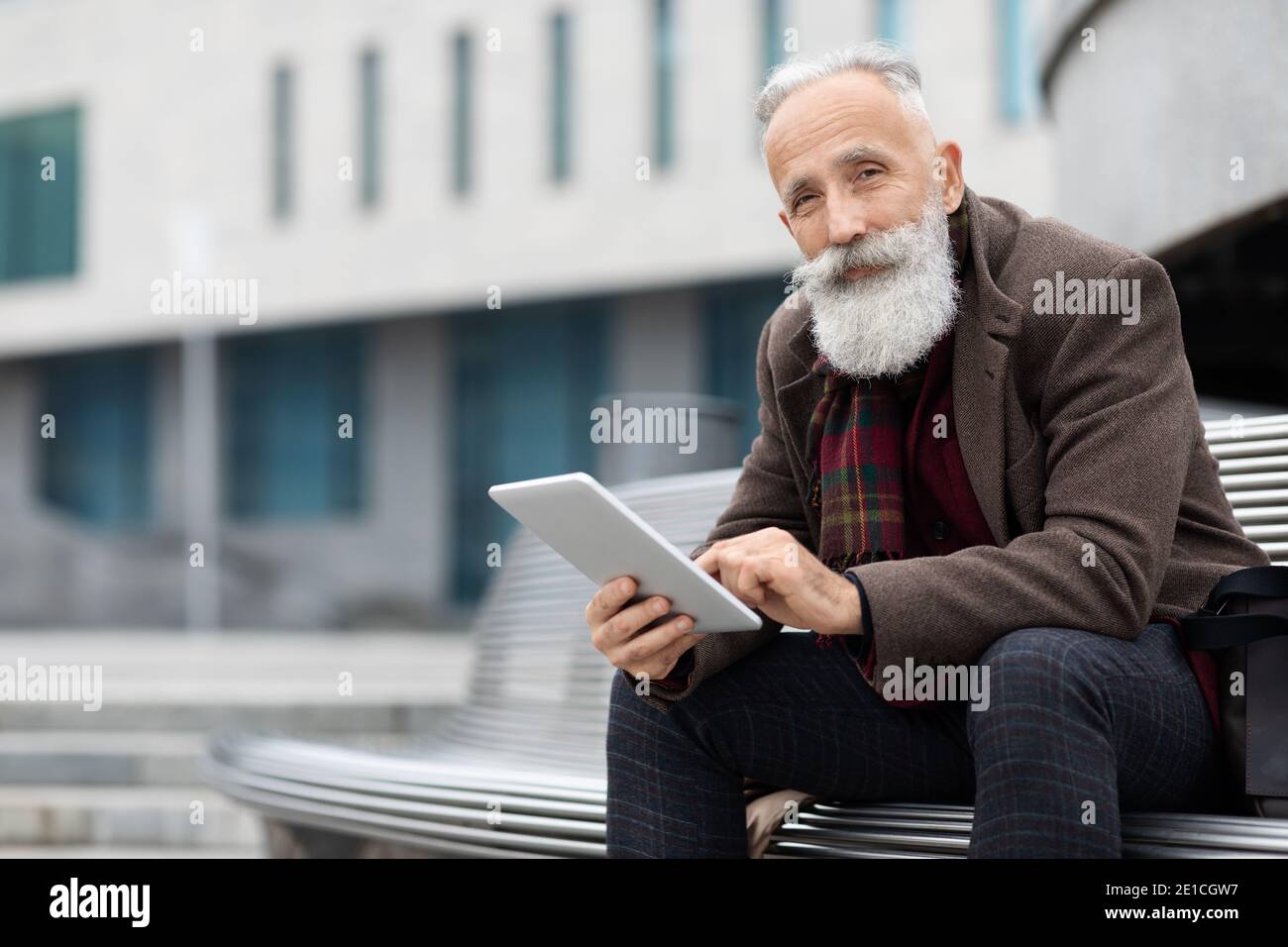 Modern aged man sitting on bench and using digital tablet Stock Photo