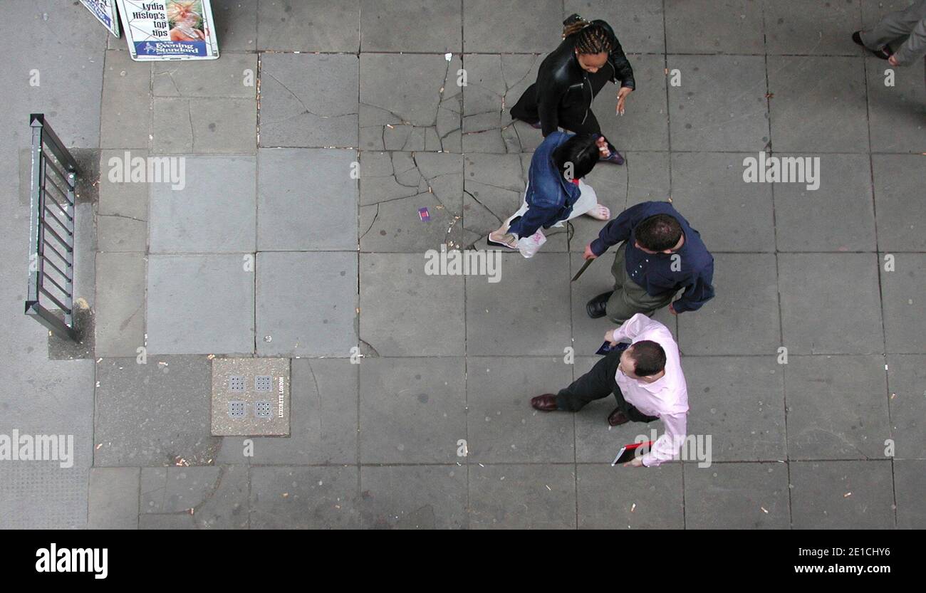 Pedestrians in City of London walking on cracked pavement with cigarette butts littering floor Stock Photo