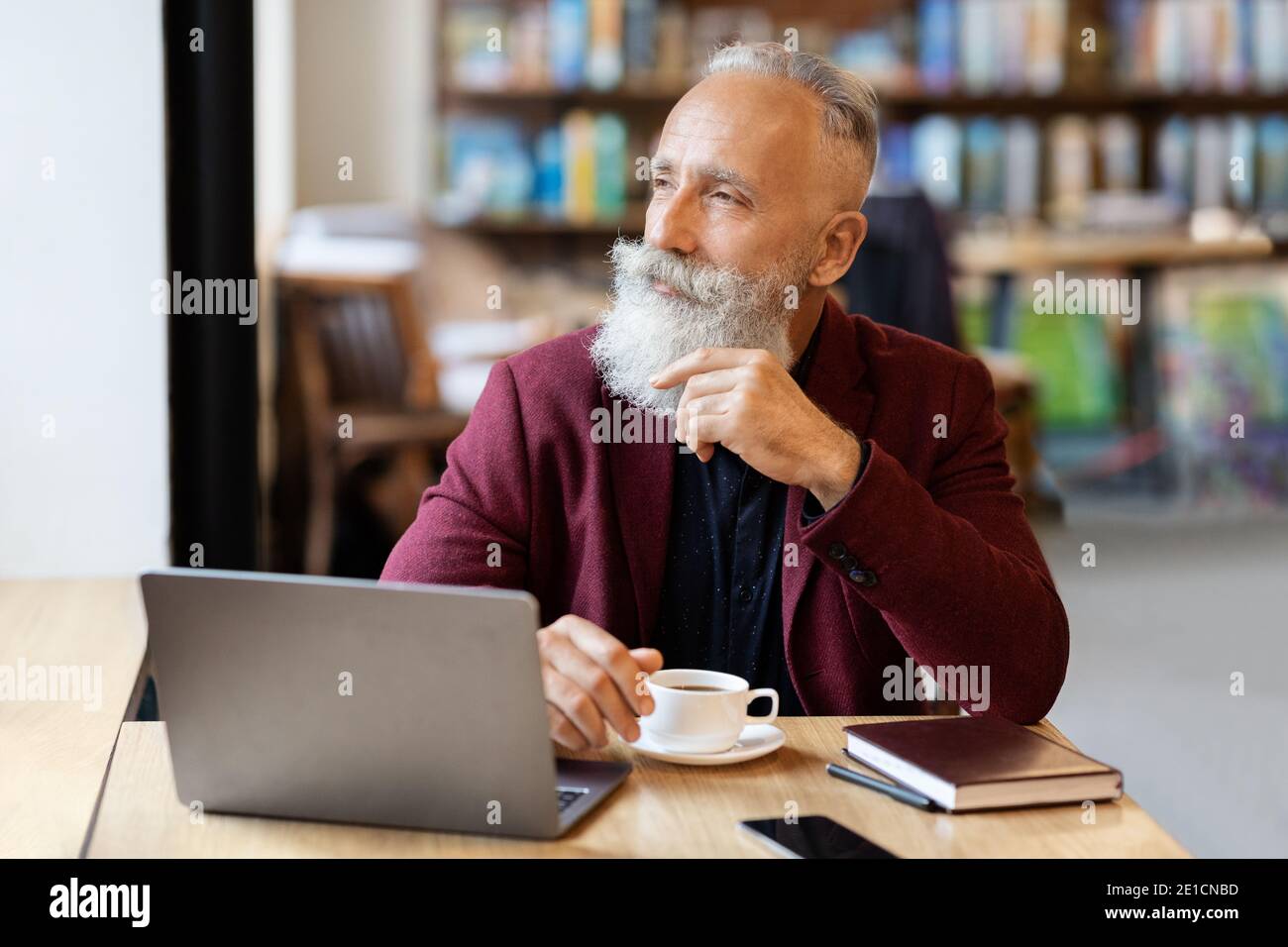 Thoughtful senior man sitting at cafe, using laptop Stock Photo
