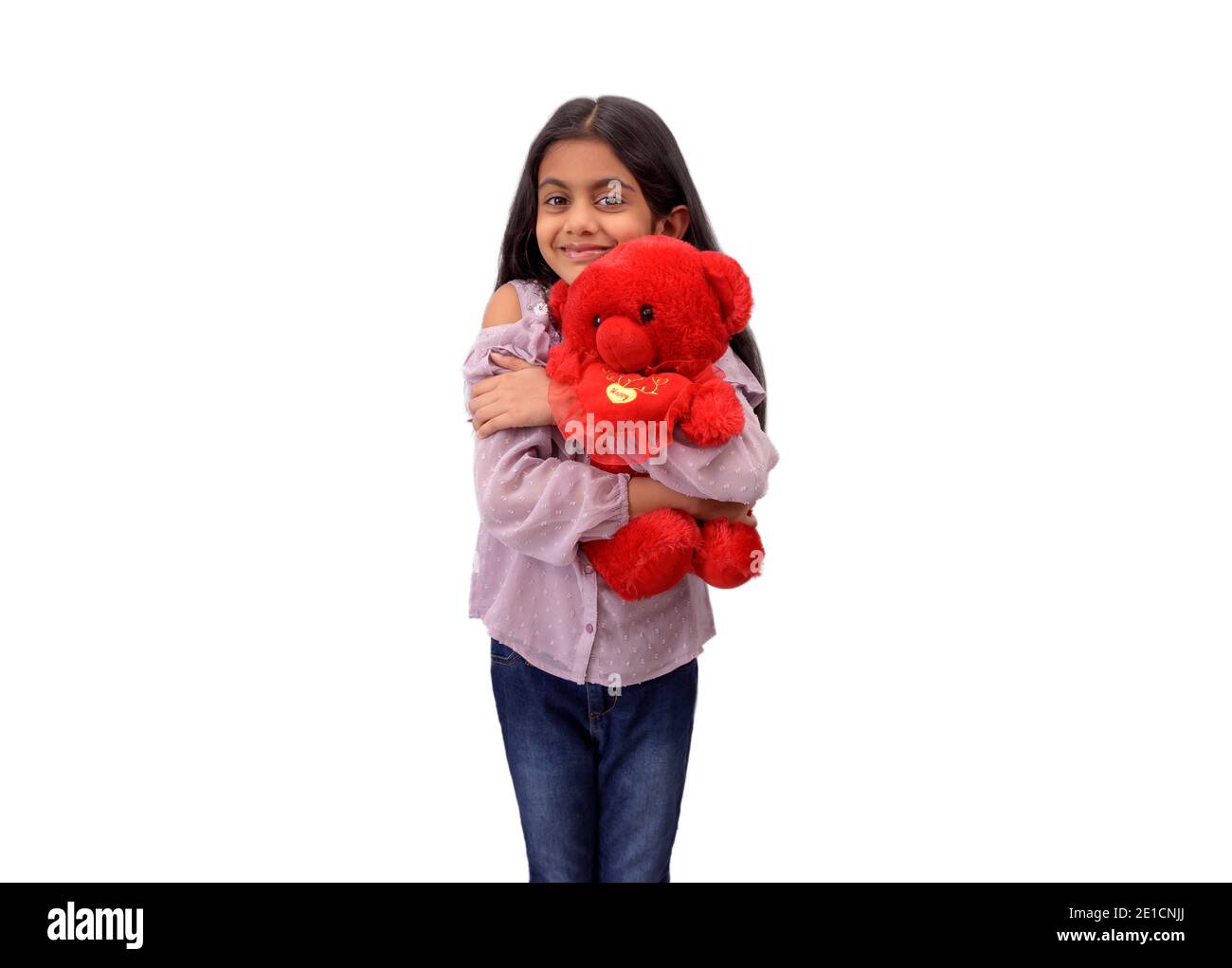 Portrait of a cute little Indian girl hugging her favourite red teddy bear and smiling in white studio background. Stock Photo