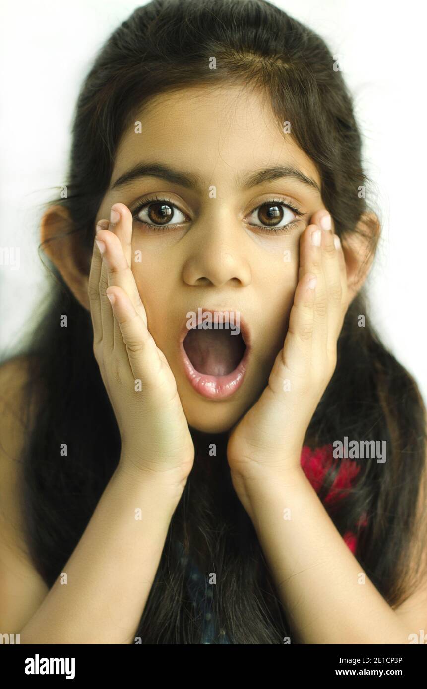 PORTRAIT OF A BEAUTIFUL INDIAN CHILD MODEL SHOWING 'SURPRISED EXPRESSION' WITH HANDS ON CHEEKS. Stock Photo