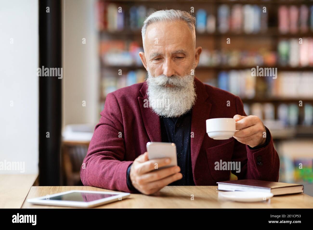 Grey-haired elderly man drinking coffee and using phone Stock Photo