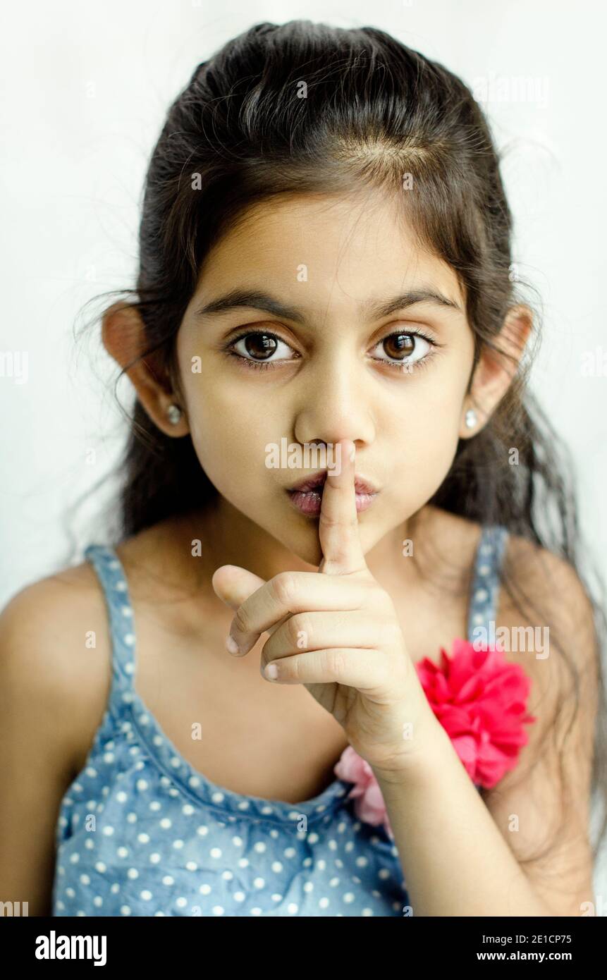 BEAUTIFUL PORTRAIT OF A INDIAN CHILD MODEL SHOWING SILENCE HAND GESTURE WITH LEFT HAND INDEX FINGER. Stock Photo