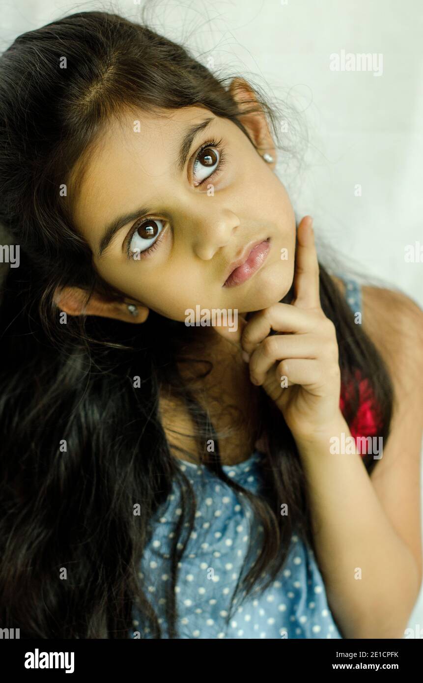 PORTRAIT OF A BEAUTIFUL AND CURIOUS INDIAN GIRLTHINKING  BY PLACING HANDS ON HER CHIN. Stock Photo