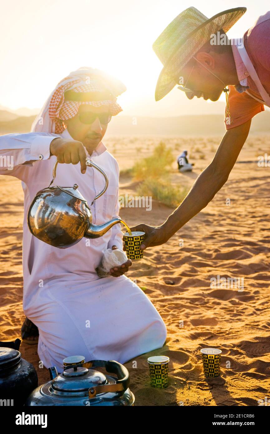 A man in traditional Arab clothing pours tea to a man in western
