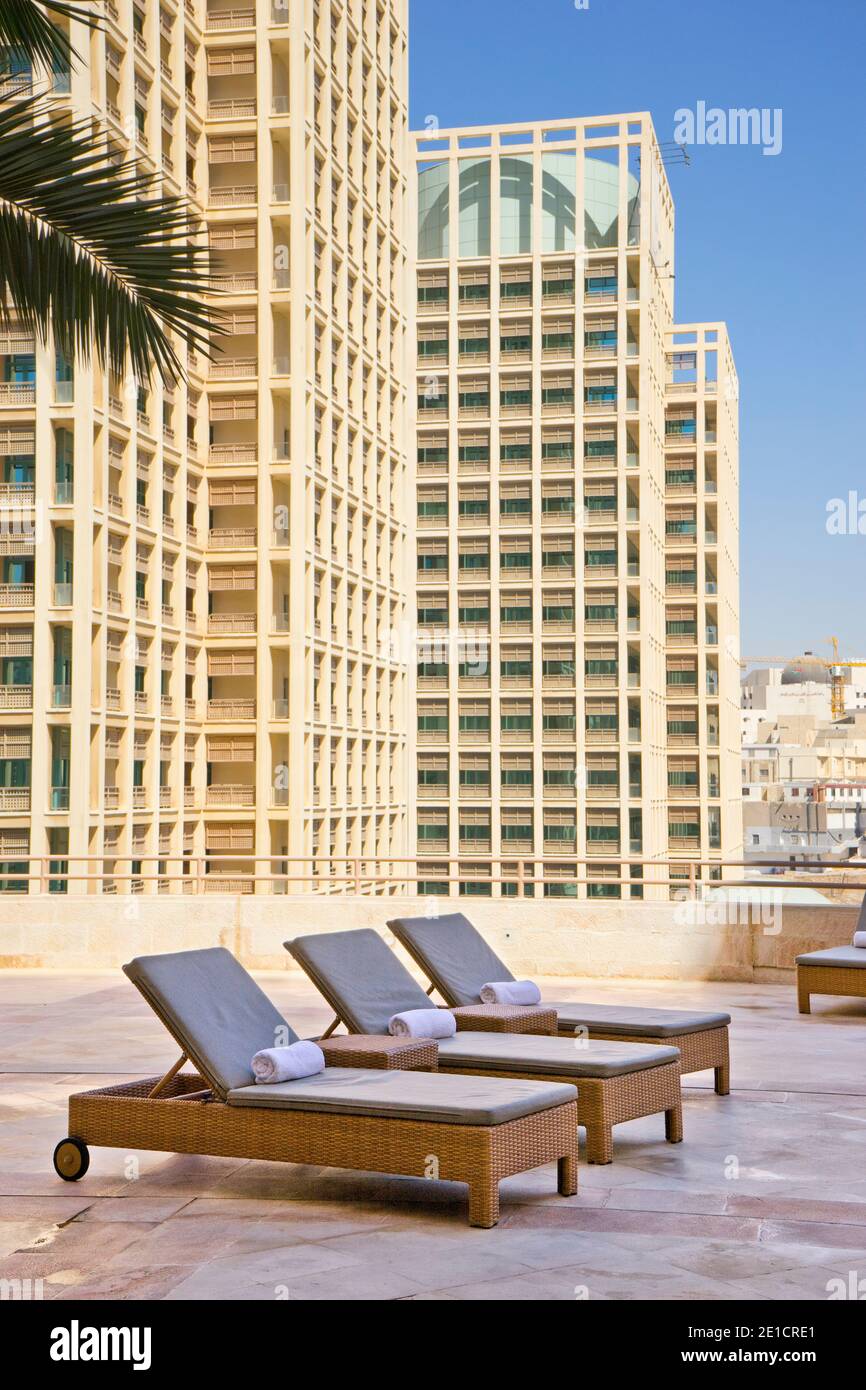 Chaise lounge chairs on a rooftop pool deck with tall city buildings in ...