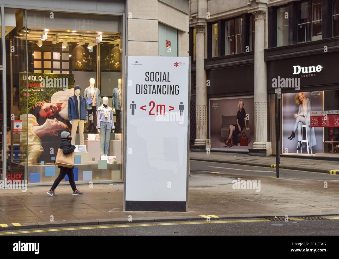 A woman walks past a social distancing sign on an empty Oxford Street in London, during the third national coronavirus lockdown in England. Stock Photo