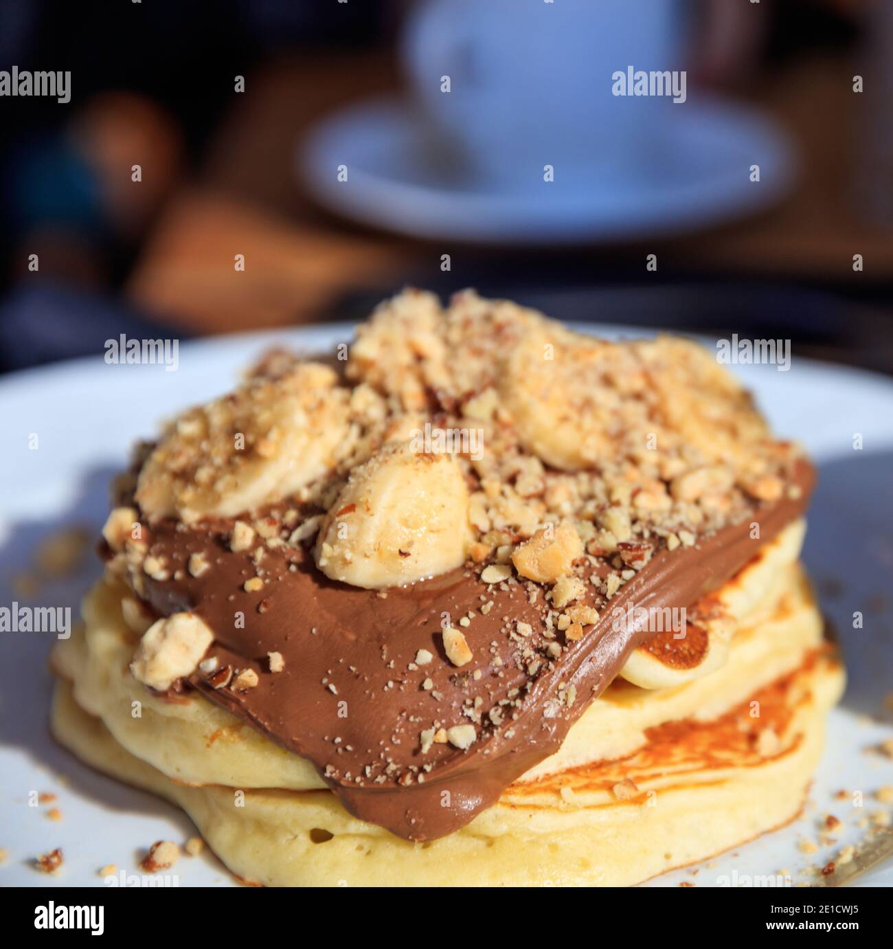 Pancakes with chocolate sauce on a white plate. Traditional American breakfast. Heap of fresh baked hot pastry with cocoa cream, fruits, walnuts. Blur Stock Photo