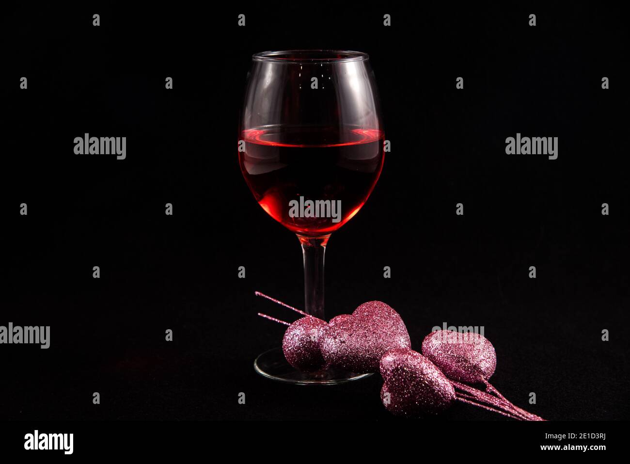 Single wine glass with Valentine hearts against a black background. Stock Photo