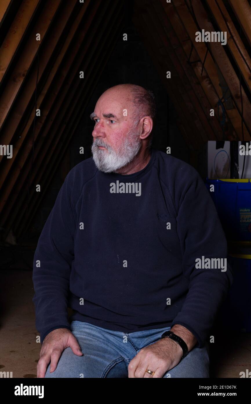Bearded old man sitting in his attic. Stock Photo