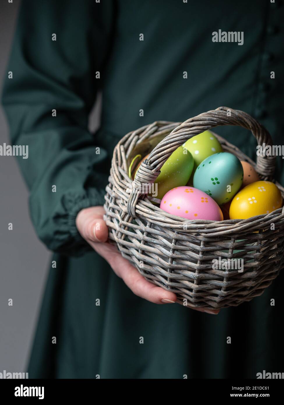 Close up of female in dark green dress holding basket of colored easter eggs. Easter concept. Dark and moody. Copy space. Stock Photo