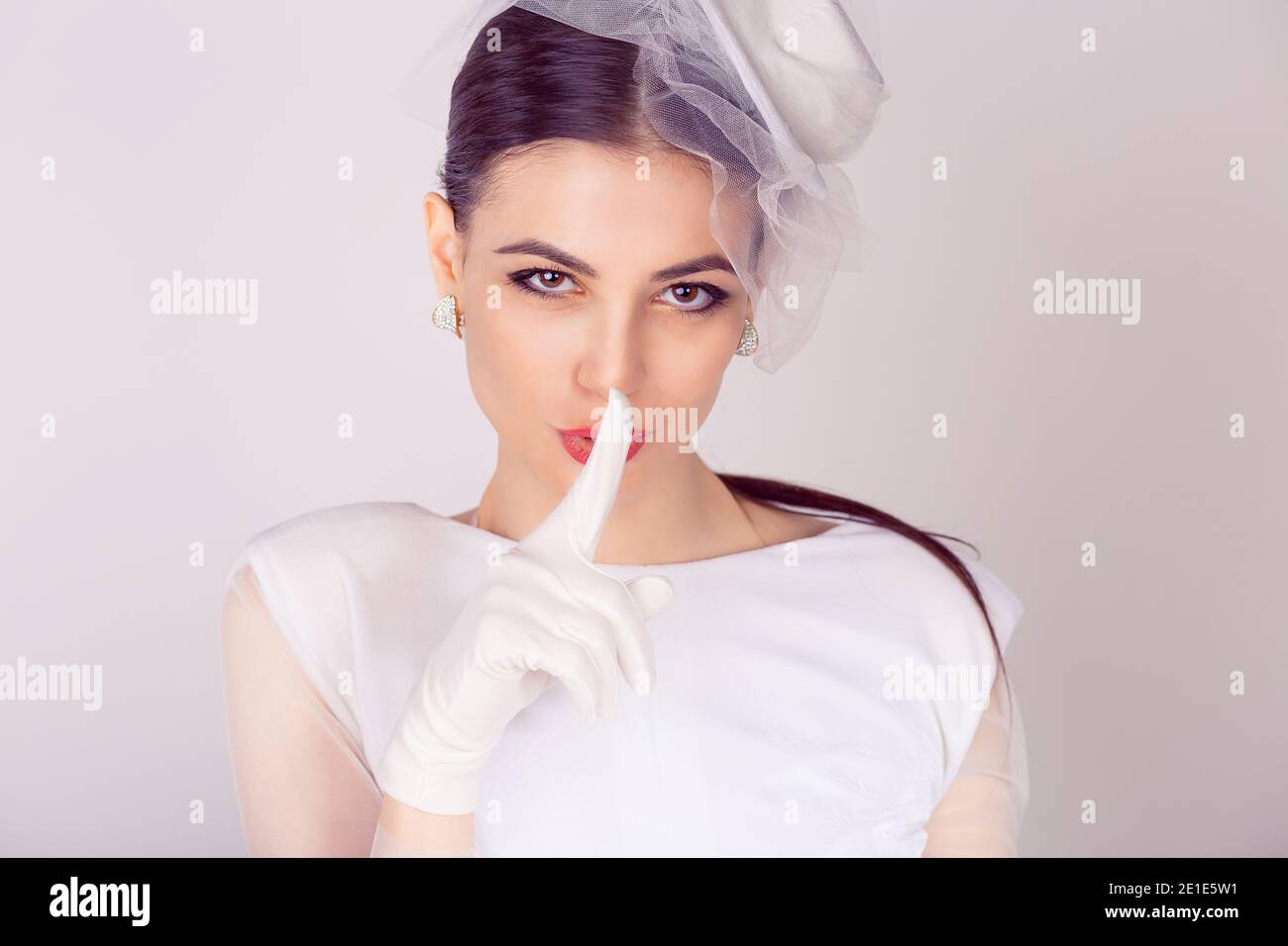 Hush. Closeup portrait picture of young woman in white dress and veil with finger on lips isolated on white gray background, keep silence concept Stock Photo