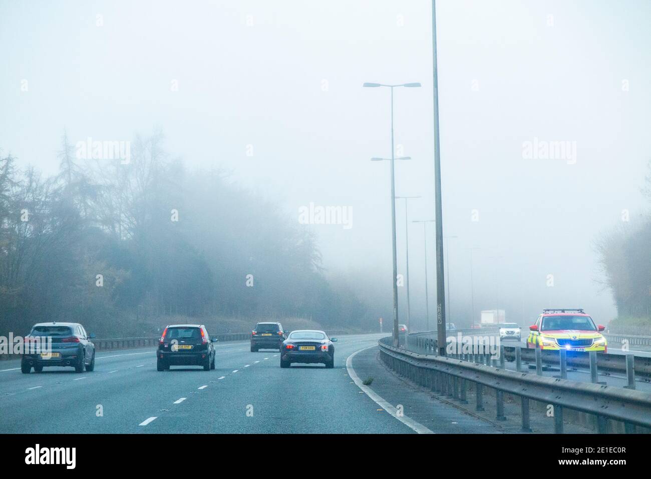 A policecar approaches in the opposite lane in foggy driving conditions