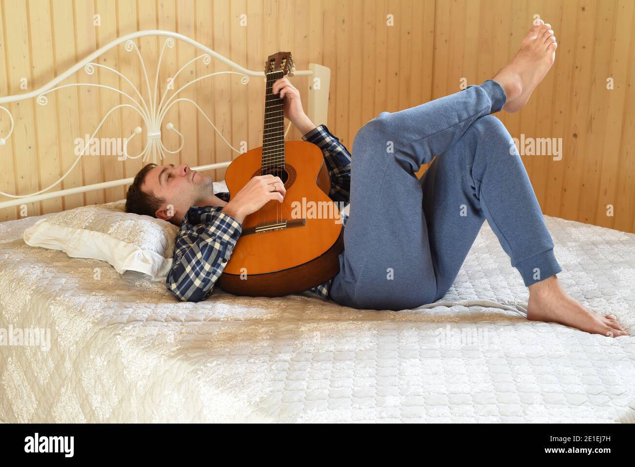 Young man playing guitar and laying on bed on weekend morning Stock Photo