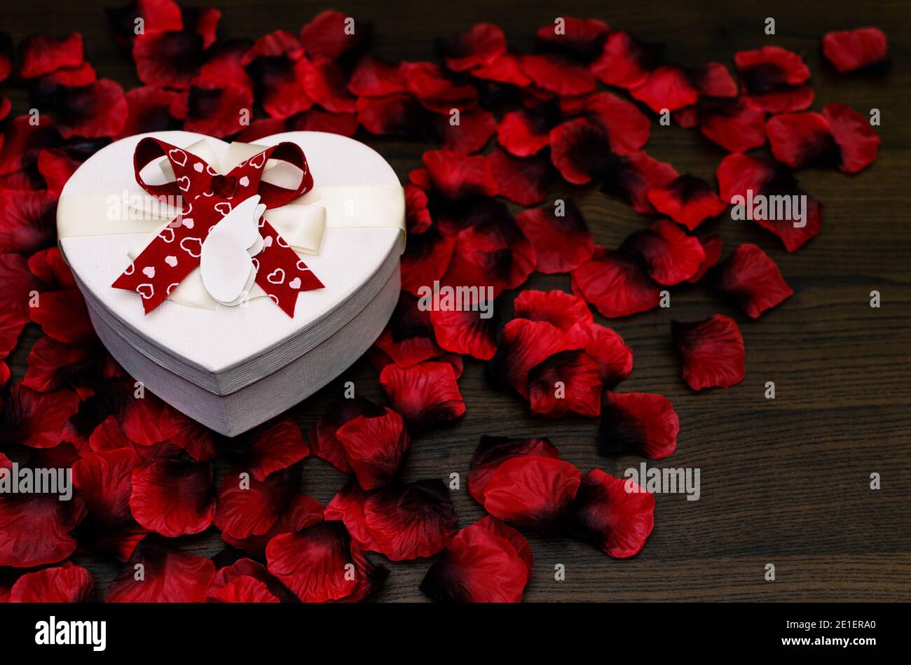 Heart shaped gift box on red roses petals and wooden table as copy ...