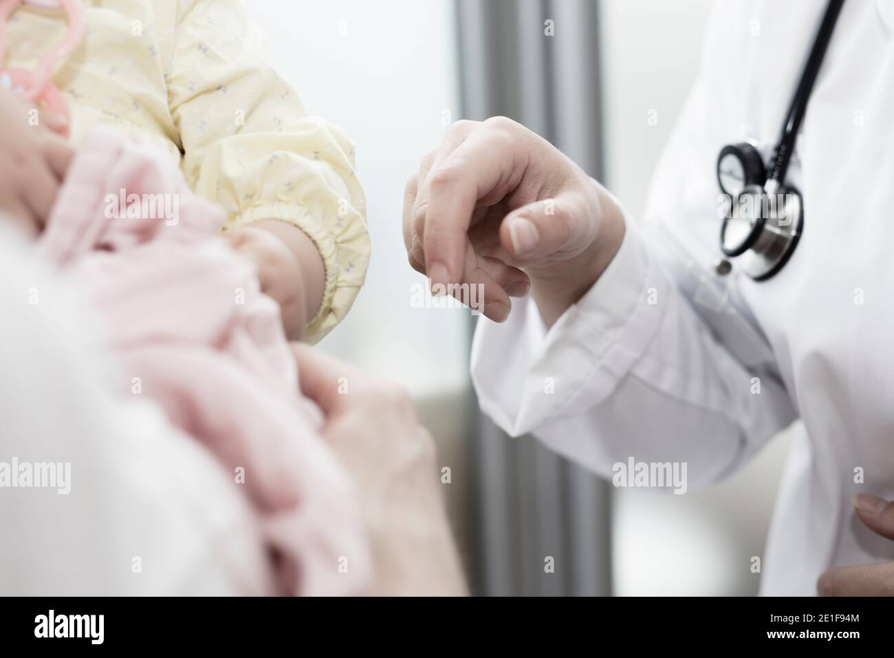 a young doctor brings her hand to a child in her mom's arms Stock Photo