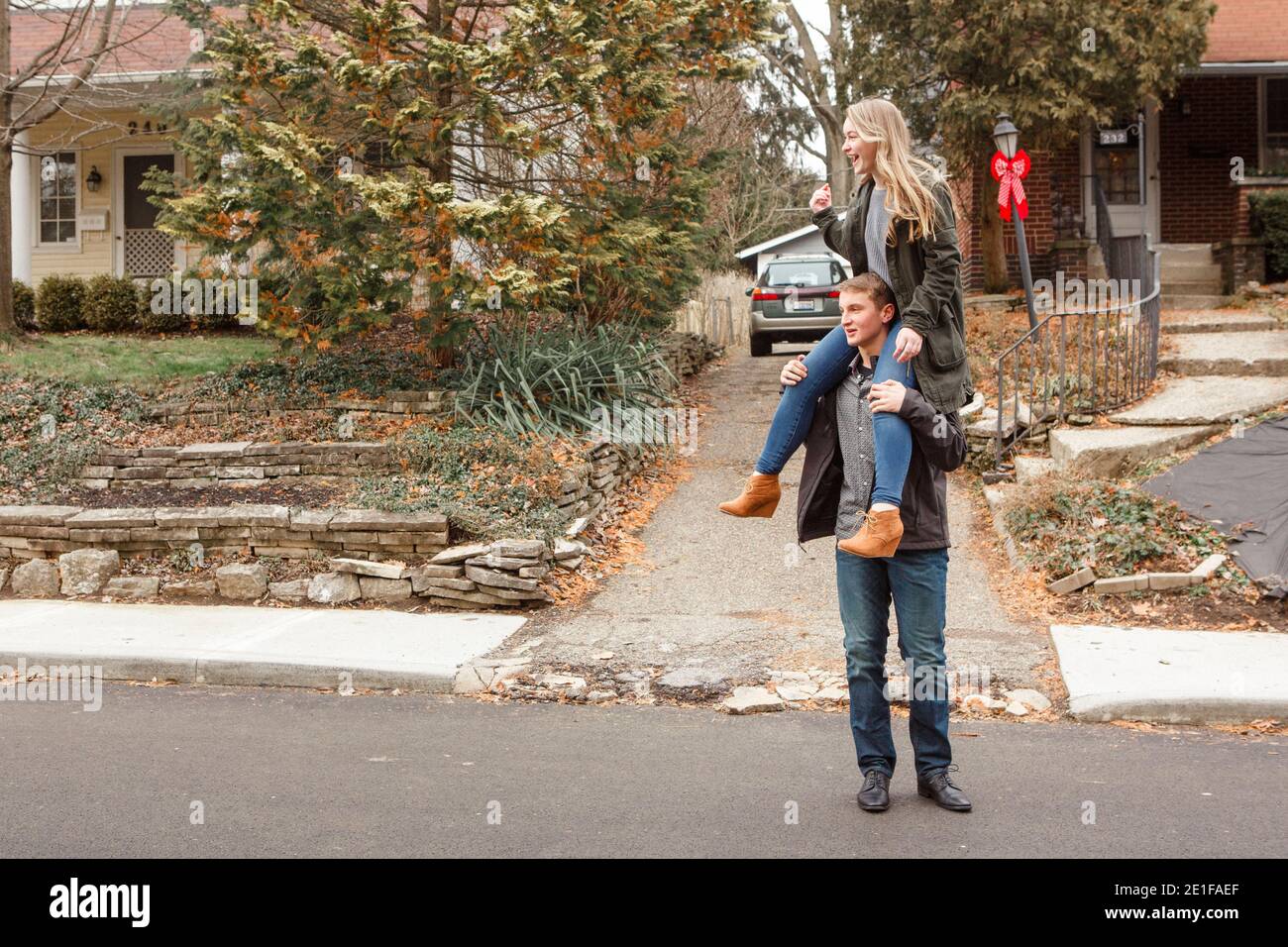 A teen brother carries his laughing sister on his shoulders on street Stock Photo