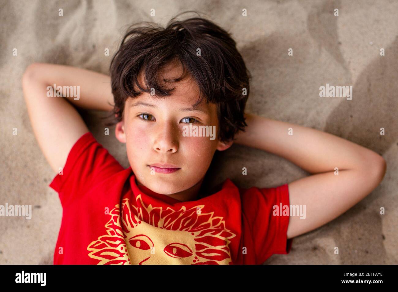closeup portrait of beautiful boy with bright eyes laying on beach