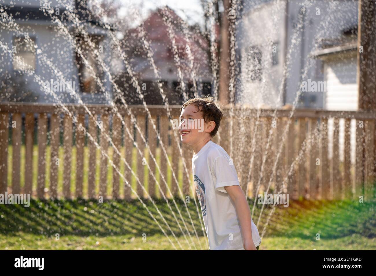 boy playing in water sprinkler in back yard Stock Photo