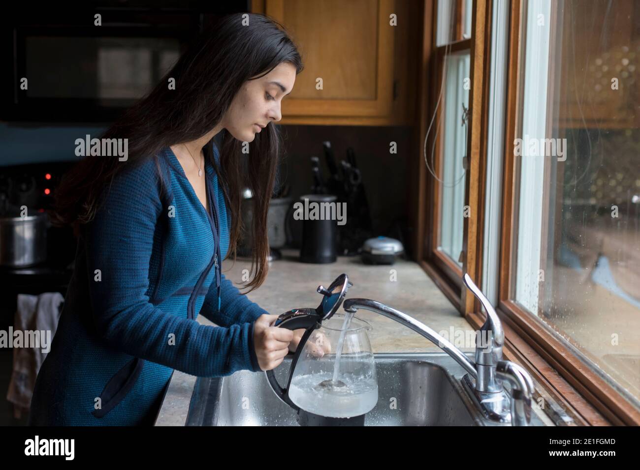 Pretty teen girl filling kettle with water in kitchen sink Stock Photo