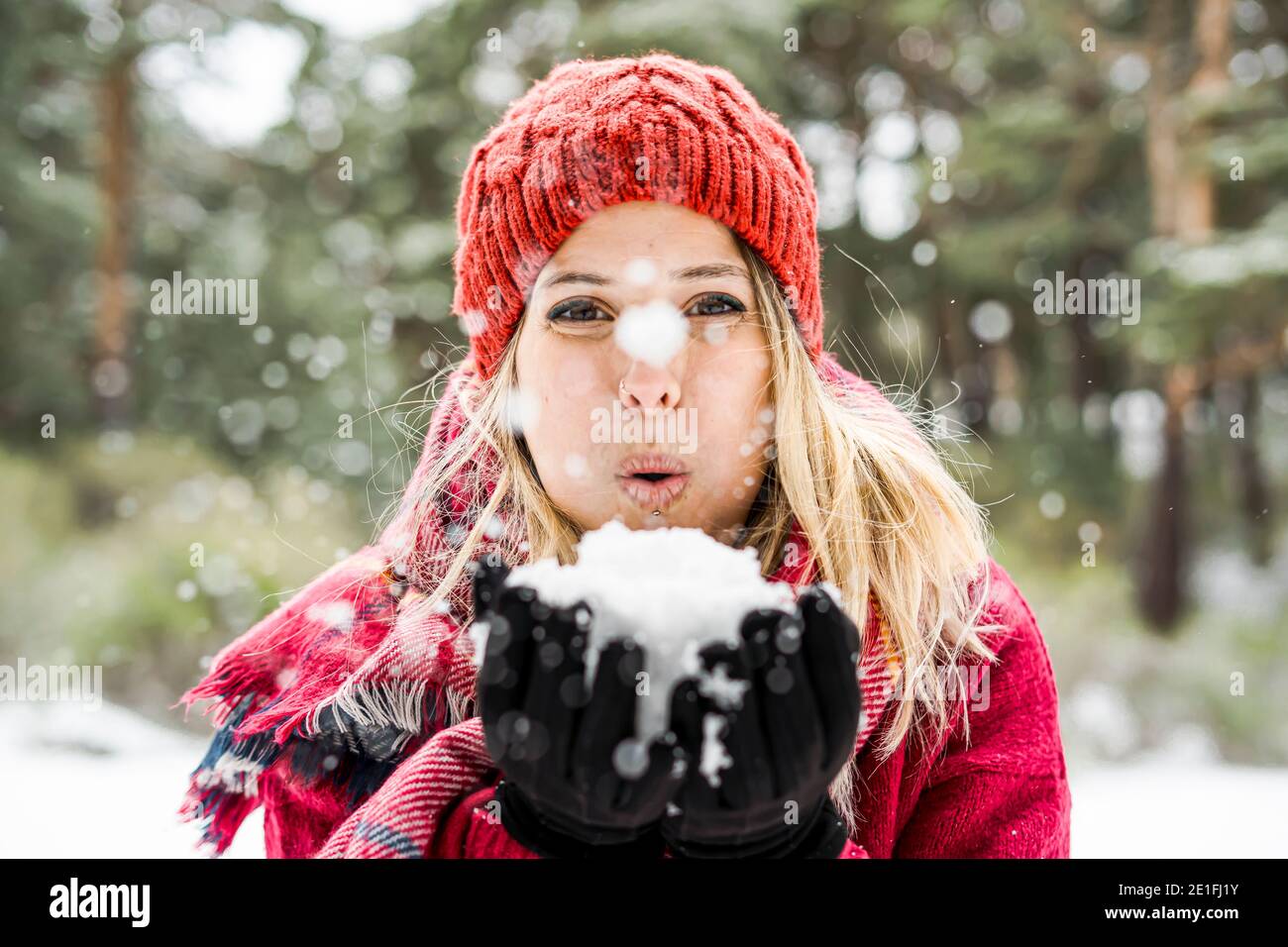 Portrait of happy young woman playing with snow in winter, blowing snowflakes to camera, copy space Stock Photo