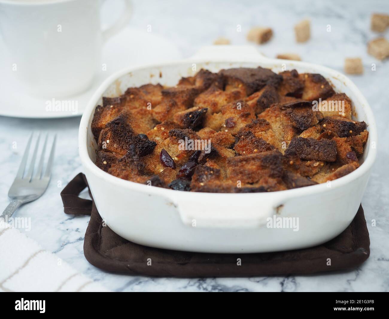 Bread pudding in white baking dish on brown heat pad with table set Stock Photo