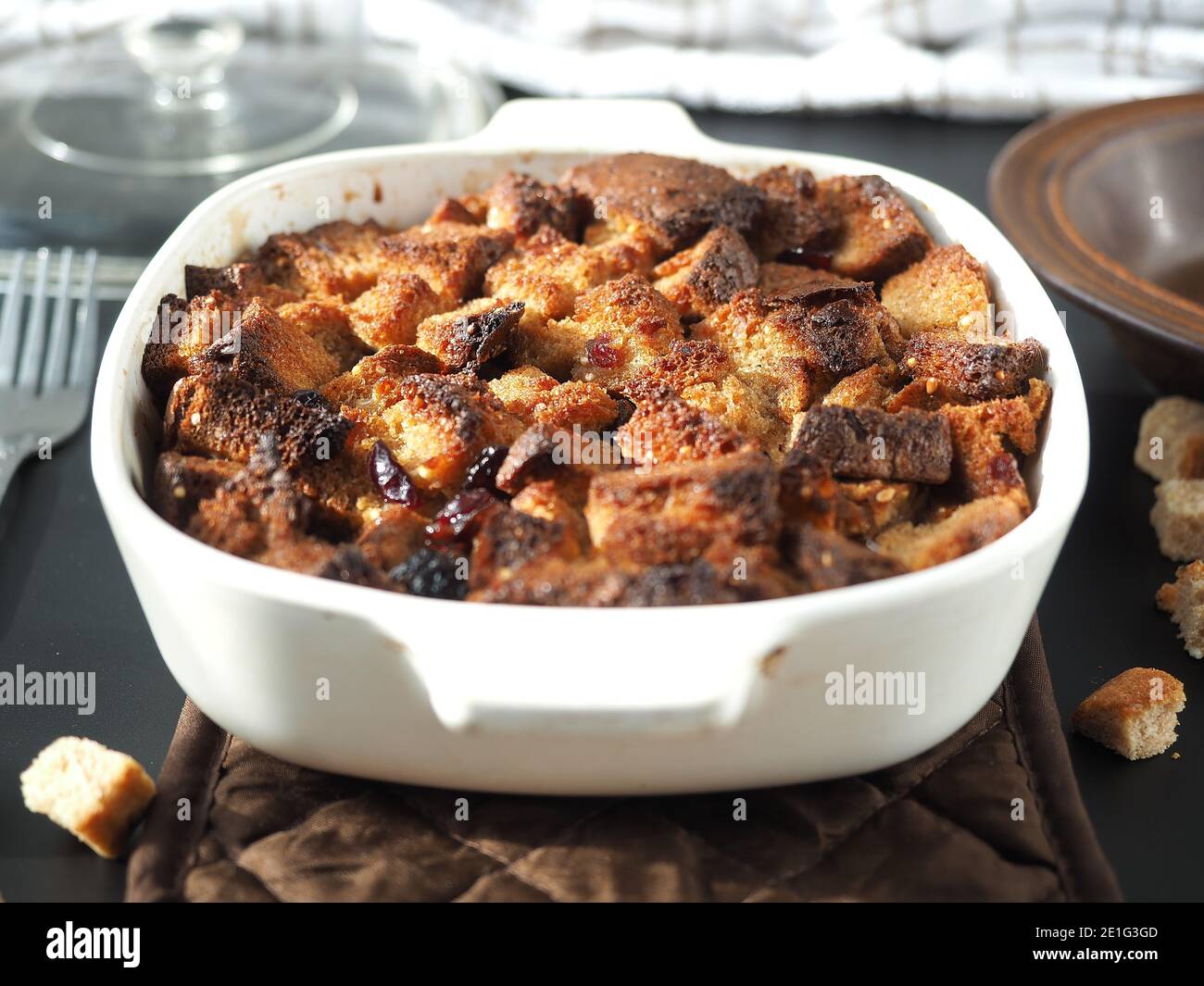 Bread pudding in white baking dish on brown heat pad with table set Stock Photo