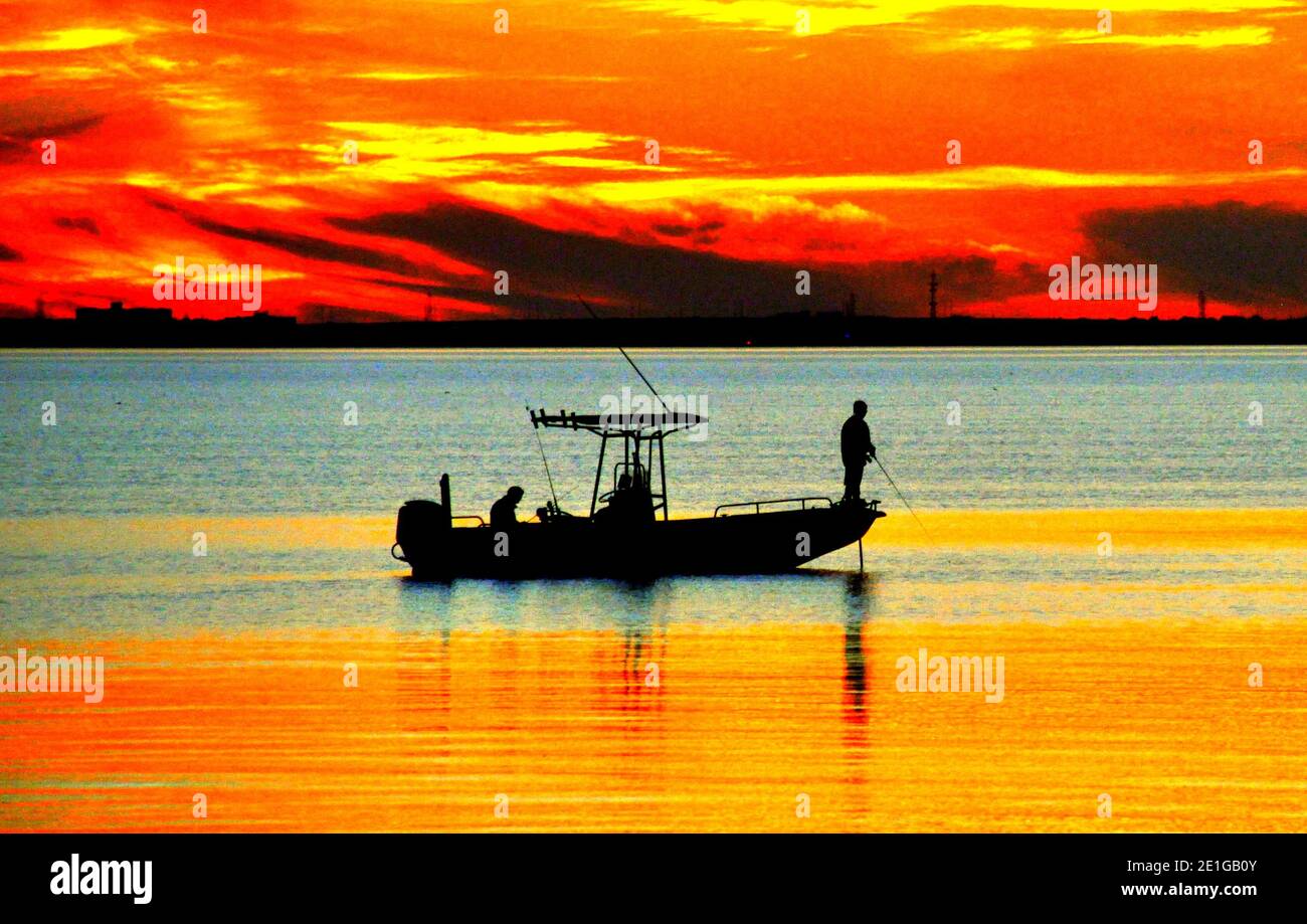 The silhouette of a fishing boat by the bay during sunrise near
