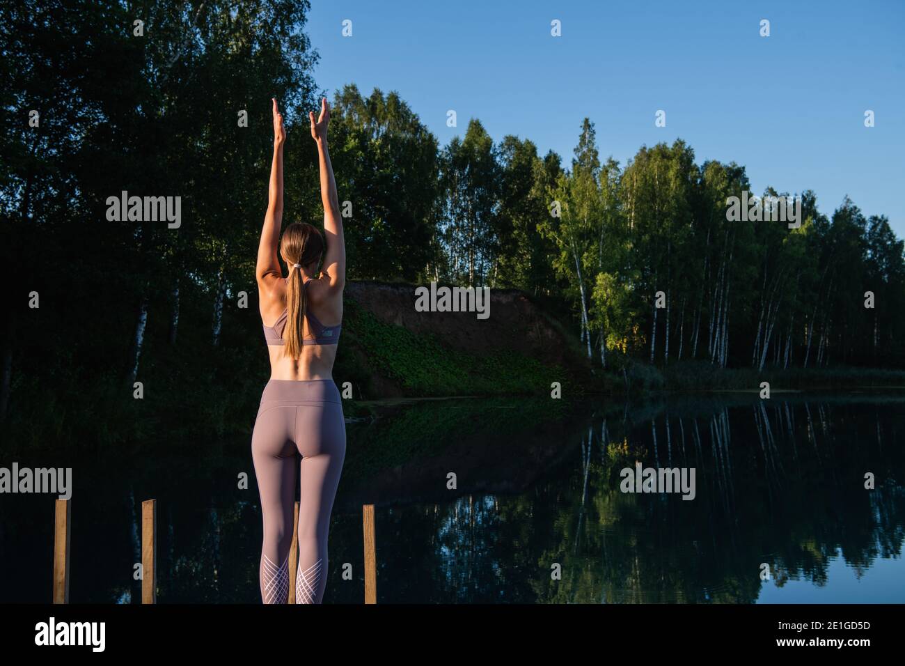 Woman doing yoga on a forest lake. Beautiful girl doing exercises on stretching and flexibility outdoors Stock Photo