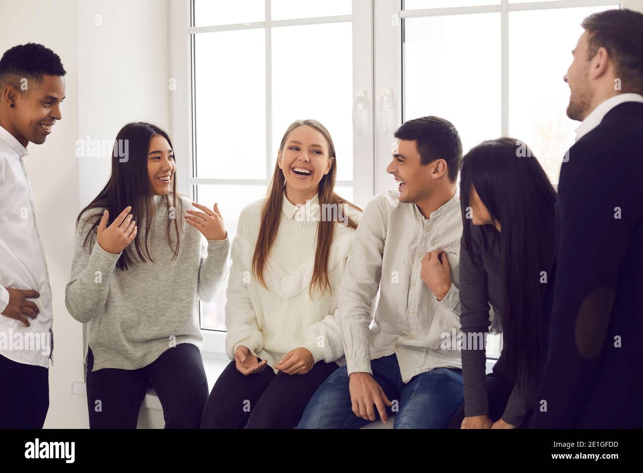 Group of happy young coworkers, students or friends talking about funny stuff and laughing Stock Photo